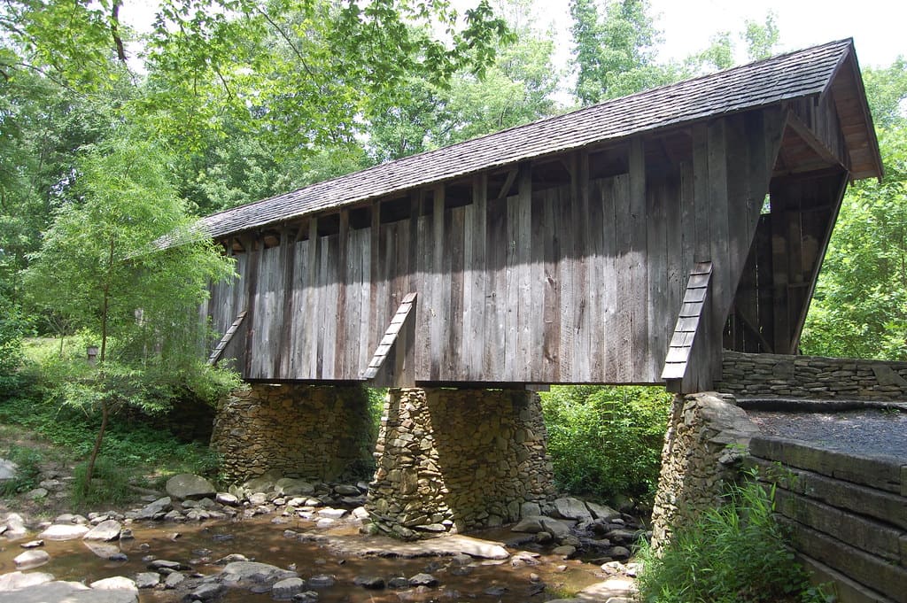 Weathered wooden Pisgah Covered Bridge over a rocky creek surrounded by green forest
